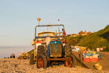 Tractors, trailers and fishing boats which make up the Cromer fishing fleet seen on the beach at sunset in the summer of 2021 on the North Norfolk coast.のeditorial素材