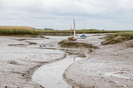 Small boats stranded off a small channel at at Brancaster Staithe on the North Norfolk coast at low tide in June 2021.のeditorial素材