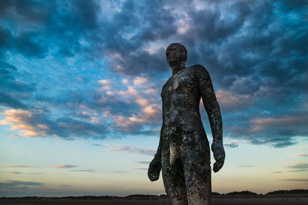 An Iron Man on Crosby beach near Liverpool towers above the beach one evening in September 2021 as he faces the sunset.のeditorial素材