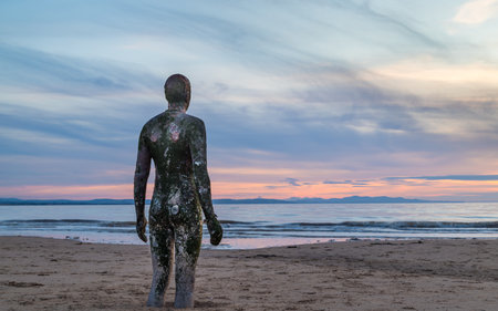 The tide coming in on Crosby beach near Liverpool in September 2021 as it approaches an Iron Man which is part of Antony Gormley's Another Place art installation.のeditorial素材