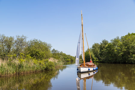 A sail boat on the calm water of the Norfolk Broads seen during the summer of 2021.のeditorial素材