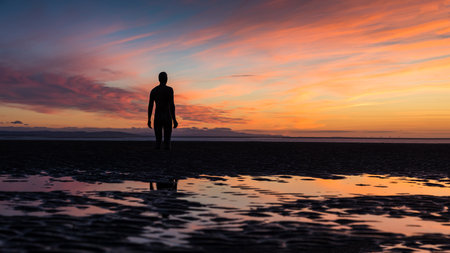 A multi image panorama of a beautiful sunset silhouetting an Iron Man on Crosby beach near Liverpool in September 2021.  He is one of the 100 Iron Men statues created by Antony Gormley which occupy this stretch of the Sefton coastline.のeditorial素材