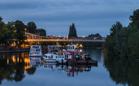 Various boats including river cruisers moored at twilight on the River Dee in Chester, under the...