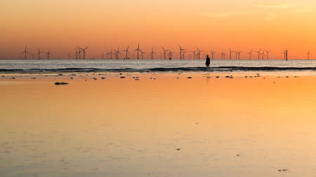 Still water behind an Iron Man forms a mirror effect at sunset in April 2021.  The statue is part of Another Place, the art installation on Crosby beach near Liverpool made up of 100 Iron Men created by Antony Gormley.のeditorial素材