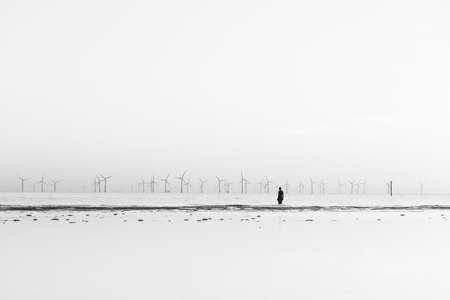 An Iron Man seen on the beach at Crosby at high tide in April 2021 facing the Burbobank wind farm.  He is part of Another Place, the art installation near Liverpool made up of 100 Iron Men statues created by Antony Gormley.のeditorial素材