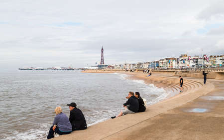 Tourists sit on the the Blackpool seafront defences watching the tide go out in September 2021.のeditorial素材