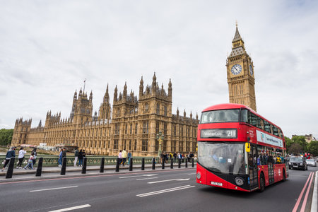 A red London bus crosses  Westminster Bridge in front of the Houses of the Parliament in London seen in May 2022.のeditorial素材