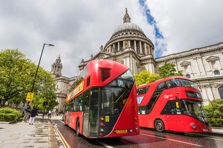 A pair of vivid red London buses pass in front of St Pauls Cathedral in the heart of London in May 2022.のeditorial素材