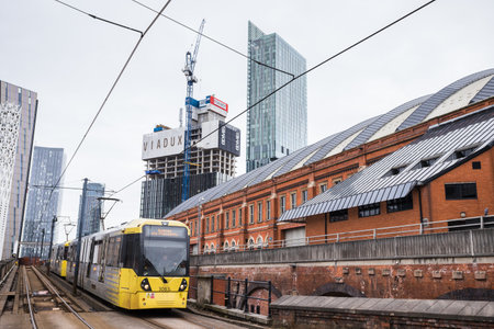 A yellow and grey Metrolink tram travelling from Deansgate into Manchester city centre in February 2023.のeditorial素材