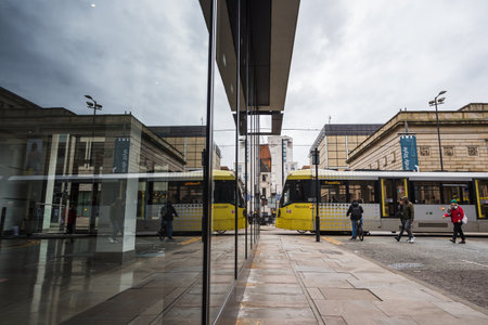 A yellow Metrolink tram reflected in the glass of a modern office building in Manchester as it travels in February 2023.のeditorial素材