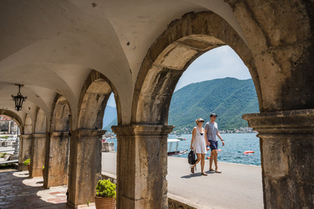 An adult couple pictured in the sunshine in May 2023 walking along the promenade and waters edge in Perast, Montenegro.のeditorial素材