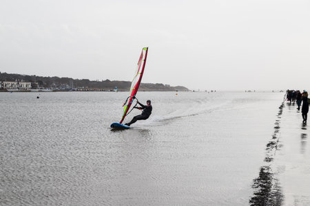 A wind surfer takes advantage of a windy day as he passes walkers at speed around the edge of the Marine Lake at West Kirby on the Wirral Peninsula on 1 January 2022.のeditorial素材