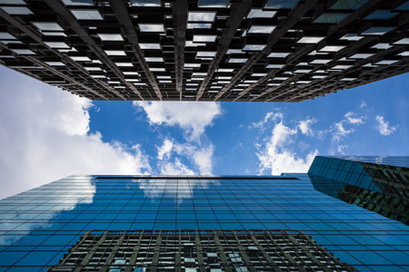 Looking towards a bright sky between two modern skyscrapers in London with clouds passing overhead.の写真素材