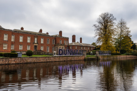 Dunham Massey Hall and Gardens reflecting in the lake with an illuminated sign ready for the Christmas lights, seen in Cheshire in November 2022.の写真素材