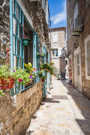 A narrow street in Budva Old Town lit up by the summer sunshine featuring flowers, window frames and limestone buildings.の写真素材