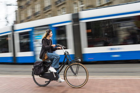 A lady on her bike is overtaken by a tram in the heart of Amsterdam, the Netherlands as she listens...