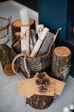 Close up of wooden logs, wicker basket, cones and candles standing on floor at cozy living room. Details at rustic design of apartment.の写真素材