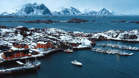 Amazing view of wooden red houses with boats among norwegian sea. Cold and dark atmosphere around. Snowy rocky mountains on distance. Beauty of Lofoten islandsの写真素材