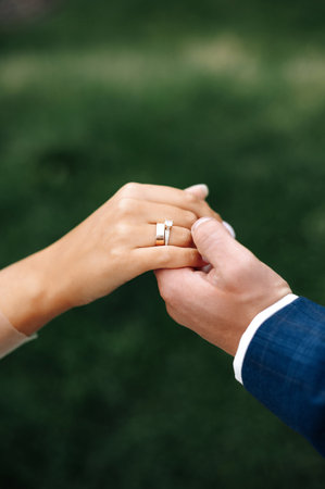 Wedding rings on hand of bride close-up. Groom gently holds the hand of his beloved on green grass backgroundの写真素材