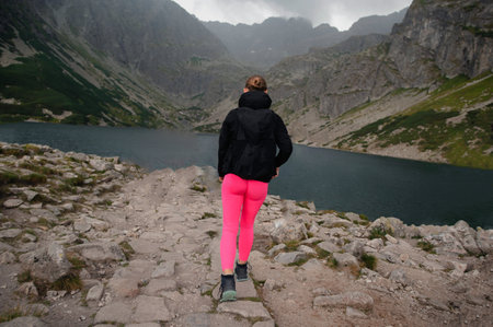Young woman in pink tights and black jacket standing on top of a mountain