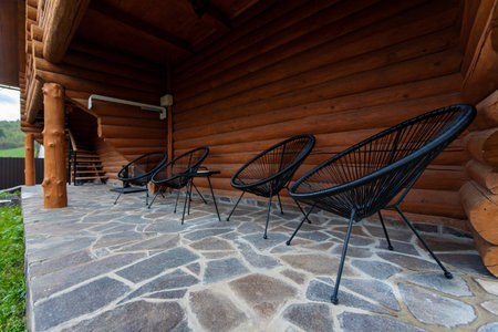 Four black wire chairs on a stone patio outside a wooden log cabin.の写真素材