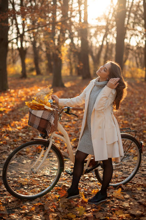 Vertical view of the happy active woman walking with bike in fall autumn park. Glad young girl in coat relaxing. Healthy lifestyle and recreation leisure activity conceptの写真素材