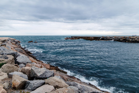 A rocky coastline with a breakwater extending into the sea under a cloudy sky.の写真素材