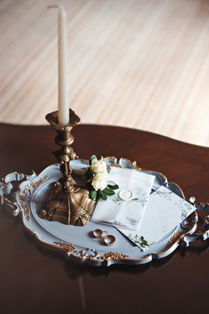 Elegant wedding invitation set on a decorative tray with a candle holder, rings, and a white flower, creating a romantic and sophisticated atmosphere.の写真素材