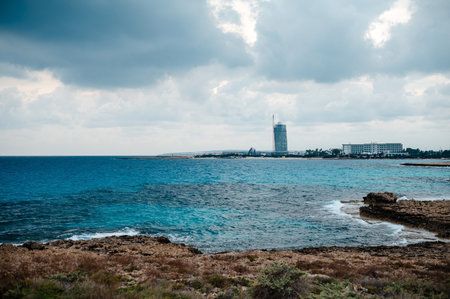 Coastal landscape with rocky shoreline and distant buildings under cloudy sky.の写真素材