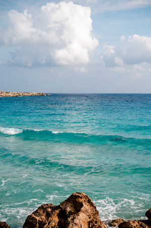 A serene coastal scene with turquoise waves gently crashing against rocks under a partly cloudy sky.