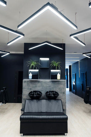 Modern hair salon interior with black and gray decor, featuring stylish lighting and sleek furniture.の写真素材