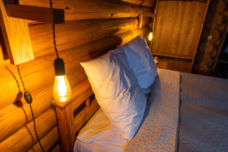 Cozy log cabin bedroom with warm lighting and a neatly made bed.の写真素材