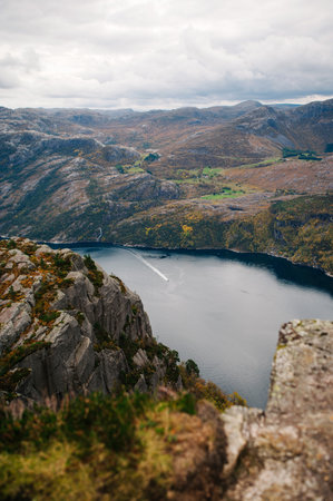 Scenic view of a Lysefjord surrounded by rocky cliffs and mountains under a cloudy sky, with a boat leaving a trail in the water. Norway, Rogalandの写真素材
