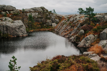 A serene landscape featuring a small lake surrounded by rocky hills and sparse vegetation under a cloudy sky.の写真素材