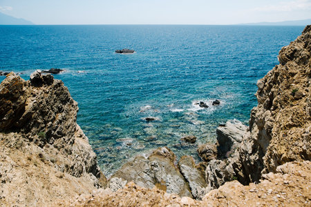 A scenic view of a rocky coastline with clear blue waters and a distant horizon. The sun is shining, creating a bright and inviting atmosphere.の写真素材