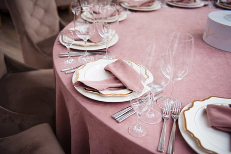 Elegant table setting with pink napkins, white plates, and crystal glassware on a pink tablecloth.