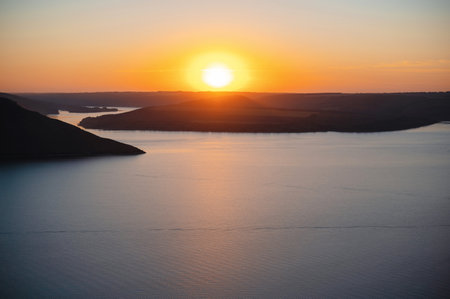 A serene sunset over a calm lake with silhouetted hills in the background.の写真素材