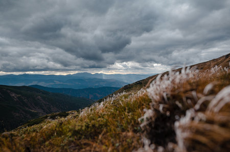 A dramatic mountain landscape with cloudy skies and frosty grass in the foreground.