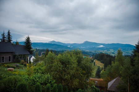 Scenic view of a mountainous landscape with houses and lush greenery under a cloudy sky.の写真素材