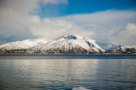 Snow-covered mountains reflected in a calm lake under a blue sky. Lofoten islands, Norway