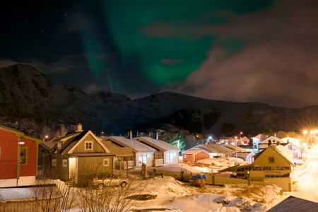 Northern lights over a snowy village at night with mountains. Lofoten islands, Norwayの写真素材