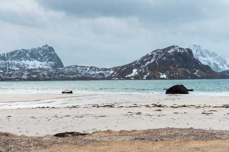 Snowy mountains and rocky beach under cloudy sky. Lofoten islands, Norwayの写真素材