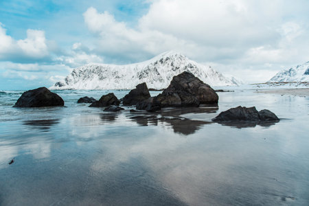 Snow-covered mountains and rocks on a reflective beach. Lofoten islands, Norway
