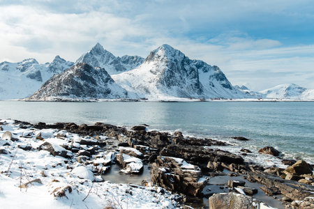 Snow-covered mountains by a calm sea with rocky shoreline. Lofoten islands, Norwayの写真素材