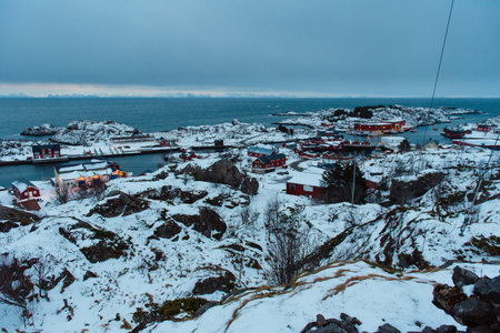 Snow-covered coastal village with red houses and rocky terrain. Lofoten islands, Norway