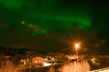 Northern lights over a small village at night, with streetlights and houses visible.の写真素材