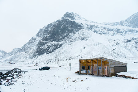 A small wooden cabin in a snowy mountainous landscape with a parked car nearby.の写真素材