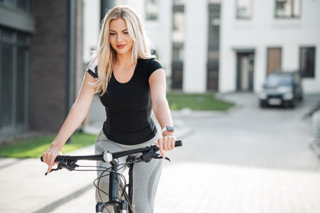 Fashion blonde woman in sports wear cycling outdoors in urban setting, smiling.の写真素材