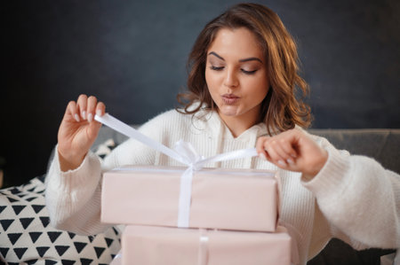 Woman unwrapping a gift box with a white ribbon, sitting indoors.の写真素材