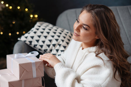 A woman in a white sweater sitting on a couch with wrapped gifts.の写真素材